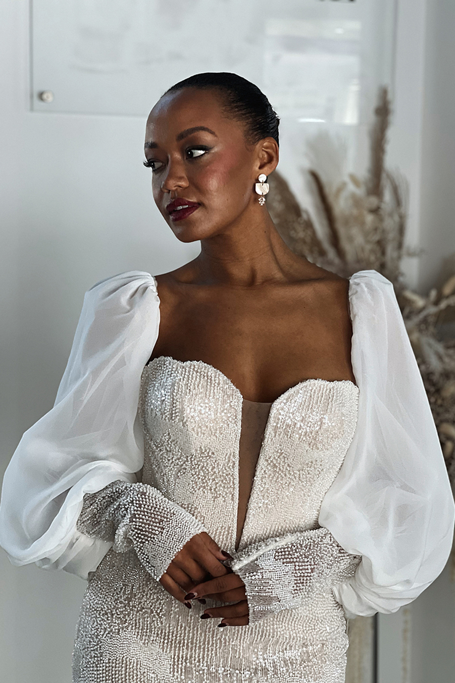 Model poses wearing beaded dress with deep v neck and dramatic balloon sleeves with beaded cuffs, image taken by Ivoura, wedding content creator.